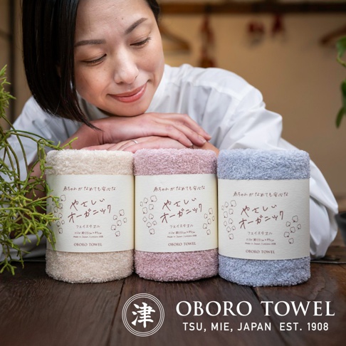 三條捲起的有機棉毛巾，分別為米白色、淡粉色和淺藍色，毛巾表面有細緻的絨毛觸感，並帶有日文標籤。