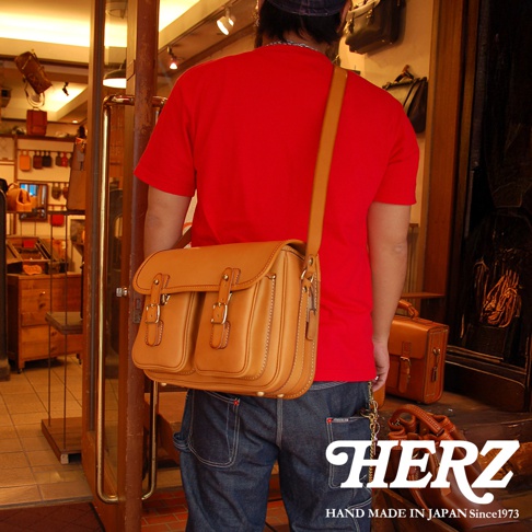日本HERZ職人手作皮革經典雙扣郵差包，以赭黃色皮革製成，搭配雙扣設計，呈現經典復古風格。