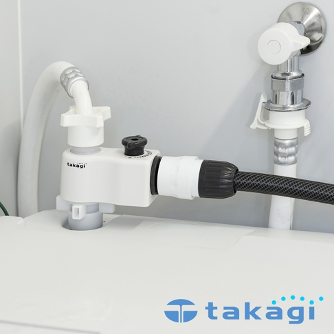 Takagi 洗衣機分水轉接頭安裝於洗衣機入水口，白色主體連接一條白色軟管與一條黑色編織軟管，右上方為連接著另一條白色軟管的金屬進水閥門，整體呈現乾淨明亮的居家水電設備場景。