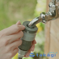 灰色與淺灰色的塑膠接頭，連接至閃亮的銀色水龍頭，背景是模糊的綠色植物。