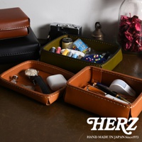 兩款職人手作皮革小物收納盒，一為棕色皮革，內有手錶、耳機、筆；另一為軍綠色皮革，內有針線、鈕扣等縫紉工具。