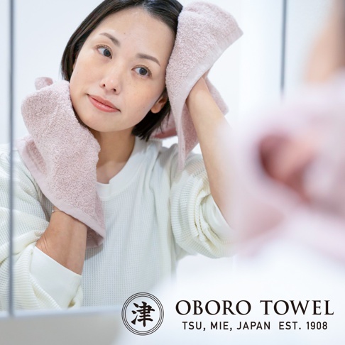 一位女性正在用粉色毛巾擦臉。毛巾柔軟，觸感細緻，材質為有機棉。