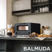 黑色BALMUDA蒸氣烤麵包機，設有玫瑰金飾邊的玻璃門、兩個旋鈕和一個開關按鈕。烤麵包機擺放在廚房檯面上，旁邊有咖啡器具和點心。