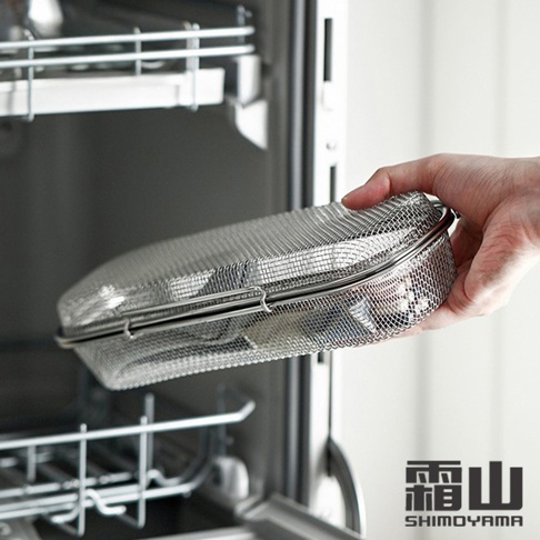 手持一個銀色 304 不鏽鋼製成的網狀清洗盒，盒身為長方形，帶有弧度，盒蓋為網狀，並有兩個金屬扣環固定。