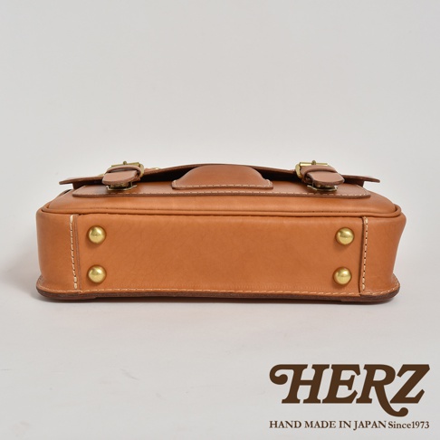 職人手作皮革傳統歐風三用學生包，展示為淺棕色牛皮材質，包身設有金色釦環、旋轉鎖扣與鉚釘，線條簡潔，風格復古。