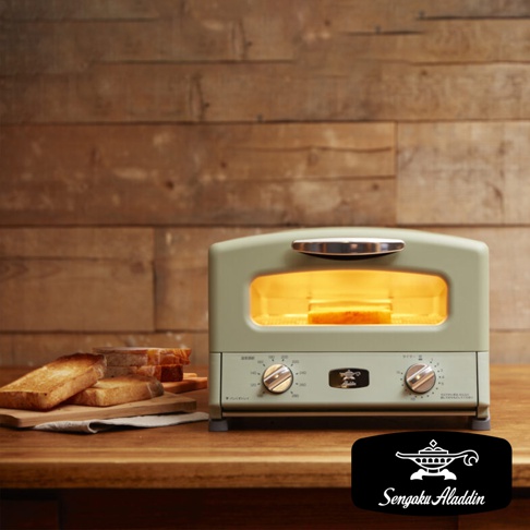 淺綠色復古多用途烤箱，配有銀色把手和兩個旋鈕，烤箱內有正在烘烤的吐司。旁邊擺放著幾片烤好的吐司，置於木製砧板上。