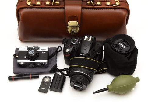 職人手作皮革橫長形杜勒斯單肩包，搭配一台黑色 Nikon 單眼相機、一台 Rollei B35 復古相機、鏡頭蓋、電池、快門線和綠色吹塵球。