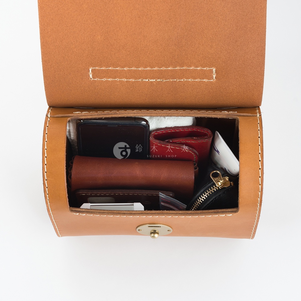 職人手作皮革復古杜勒斯手提包，頂部開蓋，內部裝有手機、紅色皮夾、棕色筆記本、黑色小零錢包和白色物品。包身為淺棕色皮革，縫線清晰可見，配有金色旋鎖。