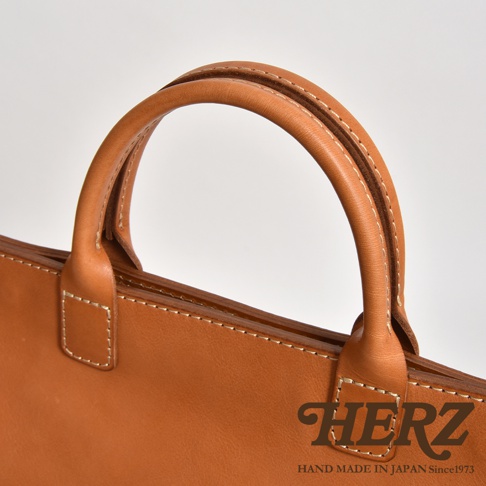 職人手作皮革大容量兩用托特包 T-8，採用光滑的棕色皮革，搭配米白色縫線，展現簡約質樸的設計。包款提把圓潤舒適，適合日常攜帶。