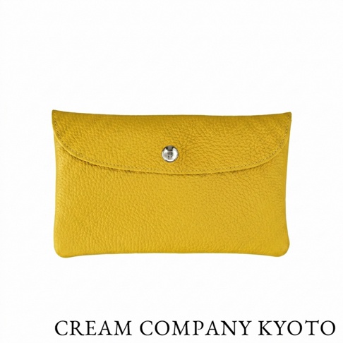 這款由京都品牌 CREAM COMPANY KYOTO 出品的黃色皮革收納包，呈現長方形簡約外觀，採用具備輕量與耐用特性的 glove 牛皮革製作。包身表面帶有細緻的荔枝紋理，中央配置一個金屬按扣，下方印有品牌名稱，整體設計精巧，適合收納名片或零錢等日常隨身小物。