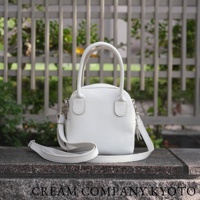 白色皮革手提包，附有可拆卸肩帶，包身呈貝殼狀，帶有雙提把和金屬配件。