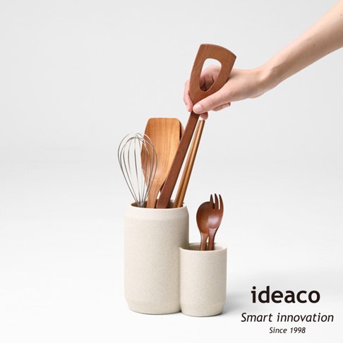 兩個不同高度的砂岩色廚具收納筒，裝有木質鍋鏟、打蛋器、筷子和木叉。