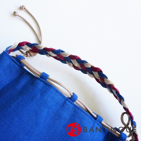 BAN INOUE 麻花辮束口手提包，藍色帆布材質，搭配紅、白、藍三色編織提把，以及米色抽繩設計