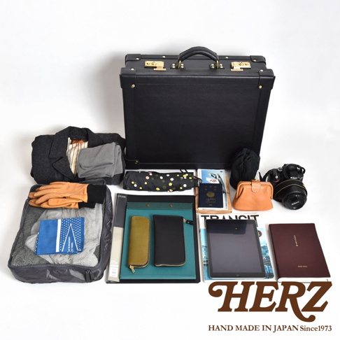 黑色皮革英倫風手提行李箱，內含衣物、文件、相機、錢包、雨傘、護照等旅行用品，搭配棕色皮革零錢包與黃色皮革長夾。