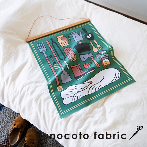 綠色帆布藝術海報，印有露營相關圖案，如水壺、鍋子、斧頭、靴子、手套、夾子、鏟子、木頭、刀子，以及一隻白色的動物。海報上方以木條懸掛，邊緣有黃色細線裝飾。