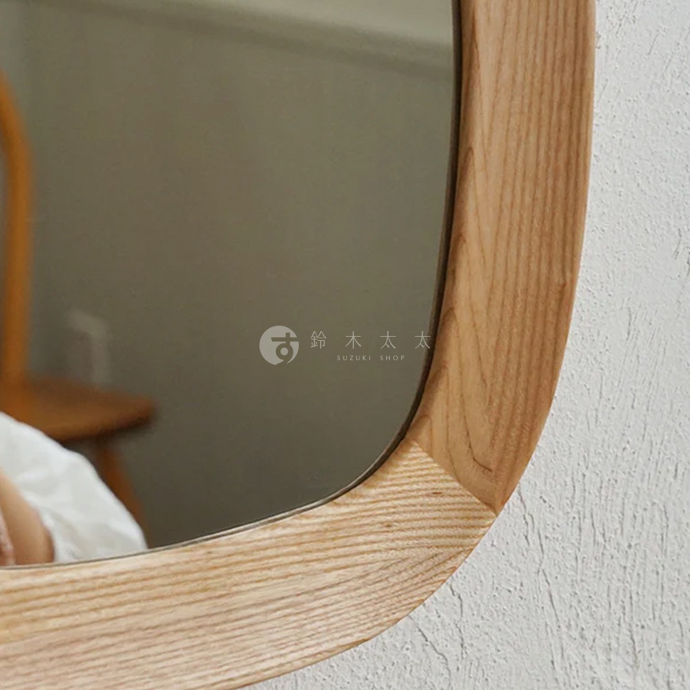 橢圓形木框壁掛鏡，淺木色天然木紋，鏡面光滑，可見背景為白色紋理牆面及模糊的室內陳設。