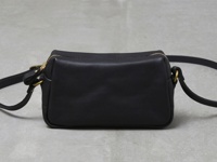 黑色皮革拉鍊單肩包，配有金色拉鍊和金屬扣環，以及可調節的黑色皮革肩帶。