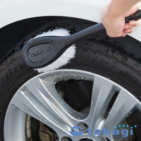 一手持黑色洗車刷，正在清潔濕漉漉的汽車輪胎和銀色輪圈。