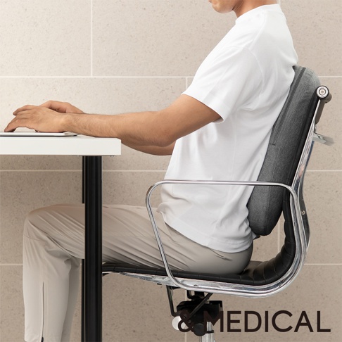 灰色布面肩頸背按摩指壓枕，固定於辦公椅椅背，支撐著一位正在使用筆記型電腦的男士。