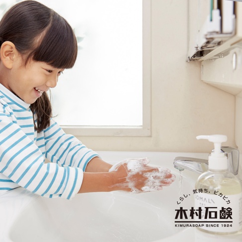 一位小女孩在水槽前洗手，手上沾滿了白色泡沫。旁邊擺放著一瓶透明瓶身的 SOMALI 洗手液體皂，瓶身標有日文和英文品牌標誌。