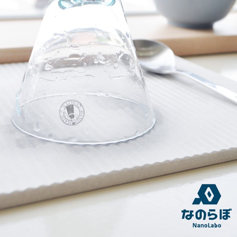 淺灰色波浪紋珪藻土置物墊，墊上有一只倒扣的透明玻璃杯，杯壁沾有水珠，旁邊放著一只銀色湯匙。