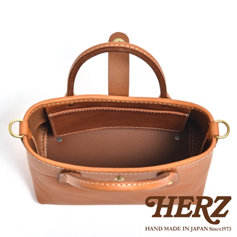 棕褐色皮革迷你托特包，頂部有提把，側面有 D 型環，內部有隔層，白色縫線，展現職人手作質感。