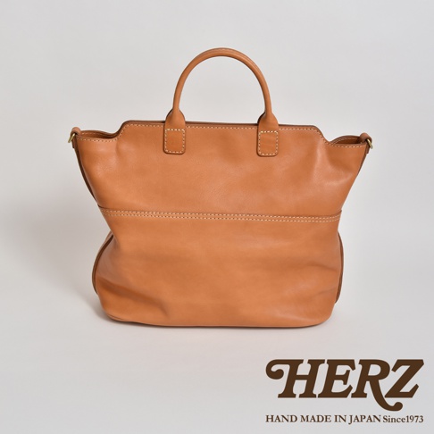 棕褐色皮革製作的職人手作托特包，包身線條簡約，結構飽滿，配有兩條短提把。包包正面有兩道車縫線，營造出立體感。