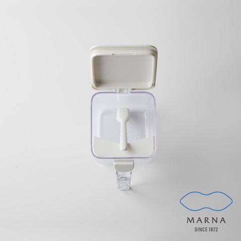 俯視視角下，一個透明的 MARNA 密封防潮調味料盒，盒蓋向上開啟，內部設有專用的白色小量匙與平整抹平架，整體設計簡約實用，右下角印有 MARNA SINCE 1872 品牌字樣與圖標。