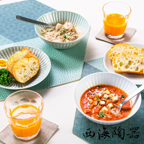 波佐見燒 FUWARI 四件式碗盤，包含兩碗、兩盤，碗盤為淺綠色調，帶有垂直條紋設計，碗內盛有雞肉蘑菇奶油濃湯和番茄燉菜，盤內則有烤麵包、水煮蛋和花椰菜，背景為藍綠色系桌墊。