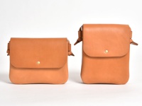 兩款不同尺寸的棕褐色皮革直式隨行袋，皆為方形翻蓋設計，配有金色按扣及皮革繫帶。