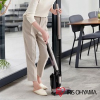 一位女士正在操作一台雙色（灰色與紫褐色）的充電式手持吸塵器，其機身與底座分離，底座為黑色，上面印有「IRIS OHYAMA」的紅色愛心標誌。