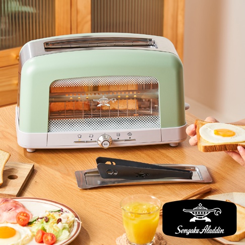 淺綠色與白色機身的烤麵包機，設有透明玻璃視窗，內部可見正在烘烤的吐司。機身前方有旋鈕和按鈕，以及Sengoku Aladdin的品牌標誌。一旁有夾著荷包蛋的吐司和沙拉。