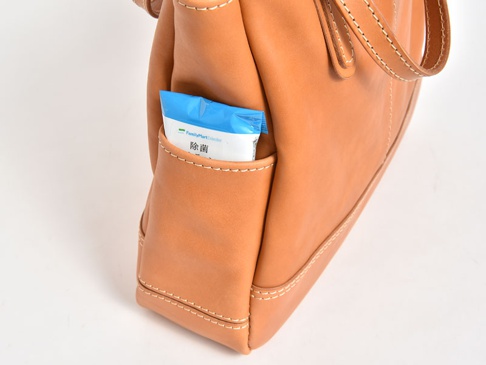 職人手作皮革直式肩背托特包，採用棕褐色光滑皮革製成，包款外部有一個小型置物袋，內有藍白色包裝的濕紙巾。