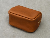 一個棕褐色的皮革拉鍊收納包，造型簡潔，材質柔軟，呈現出職人手作質感。