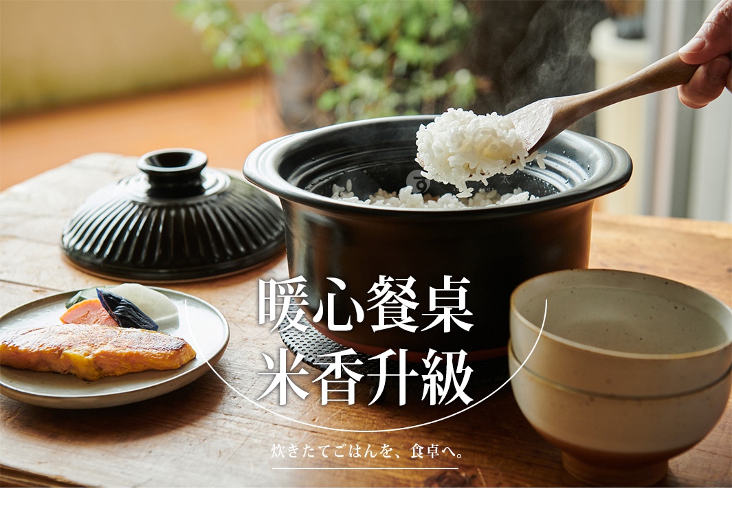以木勺盛起剛煮好的米飯，旁邊擺放著鍋蓋、裝有烤魚與漬物的盤子，以及一個飯碗，營造溫馨的餐桌意象。