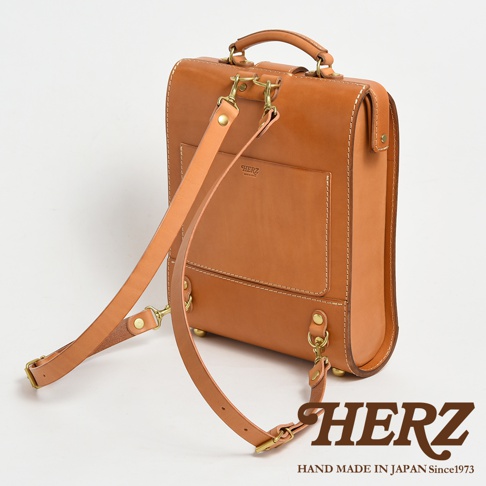 職人手作皮革杜勒斯商務後背包，淺棕色皮革製成，帶有可調節的皮革肩帶和金屬扣環。包身方形，有縫線細節和一個外層口袋，上印有品牌標誌。