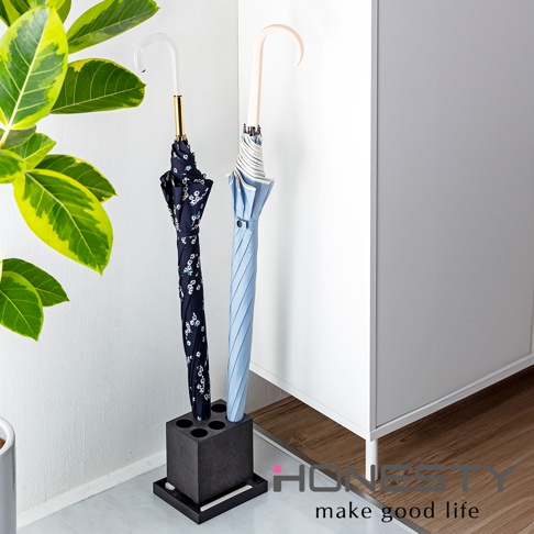 黑色珪藻土六孔傘架，可收納一把深藍色碎花傘和一把淺藍色條紋傘，傘架旁有綠葉植物。