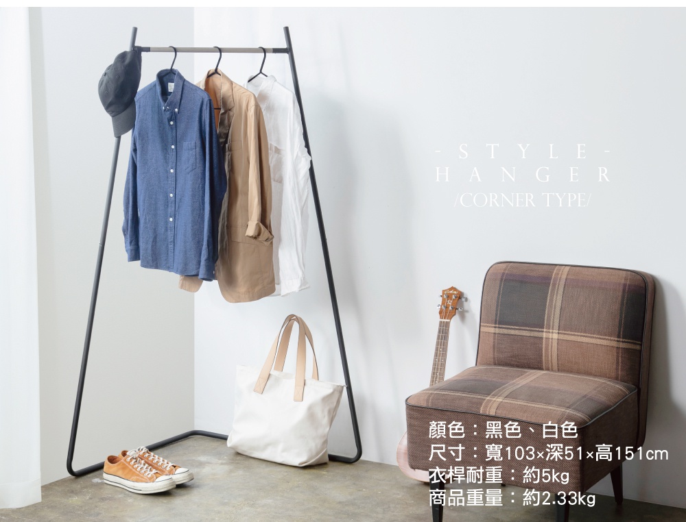 角落造型吊掛衣桿，黑色金屬框架，懸掛一件藍色襯衫、一件卡其色外套和一件白色襯衫，下方有一個白色帆布袋和一雙棕色麂皮鞋。