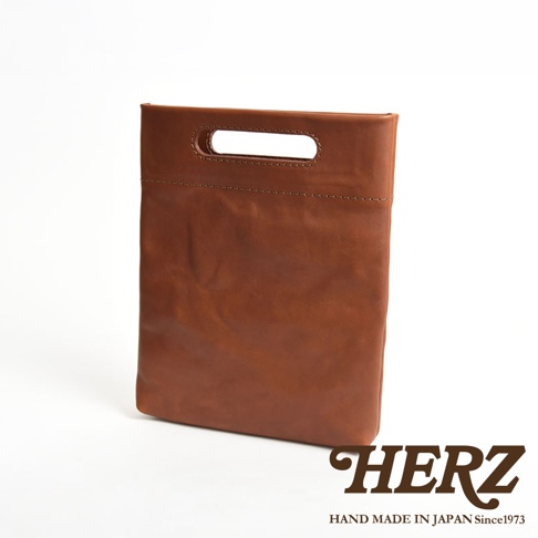 一款日本HERZ手工製作的棕色皮革收納袋，採用極簡的方正包身設計，頂部設有整合式皮革提把，整體呈現質樸細膩的質感，下方印有HERZ品牌名稱與創立年份資訊。