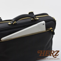 黑色皮革製成的手提公事包，設有金色拉鍊和提把，並有一個外側拉鍊口袋，其中插入一個銀色平板電腦。