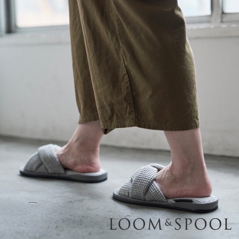 灰色交叉編織鬆餅紋室內拖鞋，鞋面為網格紋理，搭配深棕色寬褲。