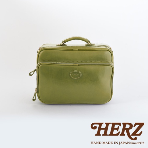 橄欖綠皮革製成的兩用商務公事包，有頂部提把及拉鍊開合，正面設有兩個拉鍊口袋，中央有品牌標誌。