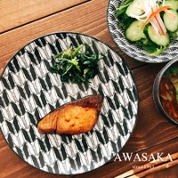 一個黑白幾何圖案的陶製料理盤，上面擺放著烤魚、菠菜和一碗沙拉。