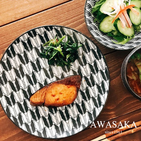 一個黑白幾何圖案的陶製料理盤，上面擺放著烤魚、菠菜和一碗沙拉。