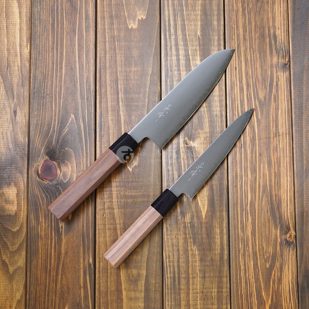 兩把景清 Chromax 鋼三德刀，刀刃呈現銀色金屬光澤，握柄為溫潤的胡桃木材質，搭配黑色連接處。