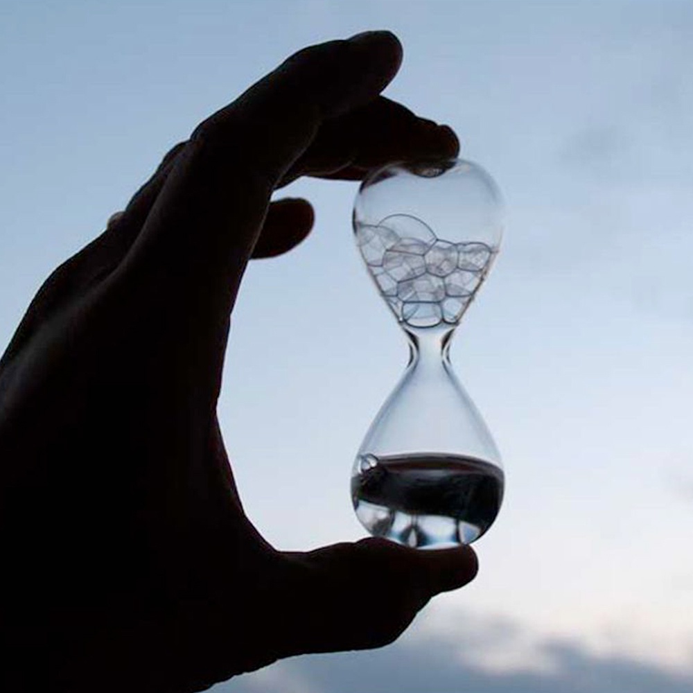 手持一個透明玻璃製成的泡泡沙漏，沙漏上半部充滿細小圓形氣泡，下半部則有少量深色液體。
