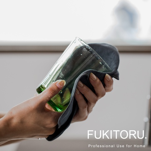 一雙手正使用深灰色超細纖維擦拭布擦拭一個綠色玻璃杯，杯上有水珠。