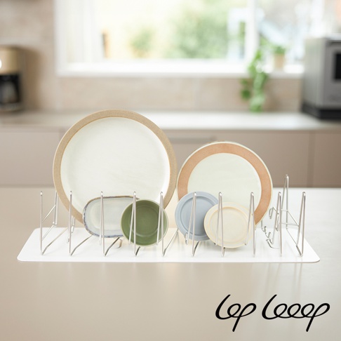 伸縮式不鏽鋼瀝水架，配有白色防水墊，架上擺放著多個陶瓷盤，包括一個大白色盤，一個帶有棕色邊緣的盤，以及幾個小尺寸的綠色、藍色和白色盤。