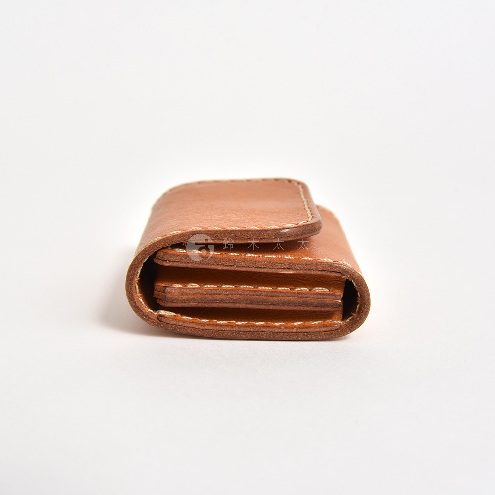 這是一款由日本品牌HERZ職人手作的棕色Stare皮革雙折零錢包，從側面視角呈現，展示了其細緻的縫線工藝、層次分明的皮革疊層設計與簡約的折疊結構。