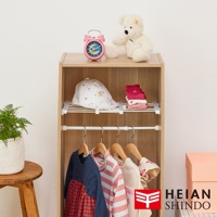 平安伸銅全功能伸縮縫隙置物架 SMR-24，展示架上擺放著可愛的粉紅色鬧鐘、白色櫻桃圖案的帽子、粉色疊放的襪子，以及可愛的白色泰迪熊。架子下方懸掛著幾件嬰幼兒衣物，包括一件深藍色和紅色格紋連身裙，以及粉白條紋上衣。旁邊還有粉色禮盒和綠色盆栽植物，下方角落印有 HEIAN SHINDO 的 Logo。